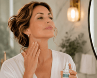 Thumbnail for A woman in a white robe applies a skincare product from a small silver bottle to her neck, standing in front of a mirror in a softly lit bathroom.
