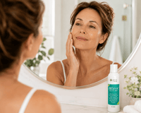 Thumbnail for A woman looks into a round bathroom mirror while touching her face, with a bottle of Biozyme enzyme peel placed on the counter in the foreground.