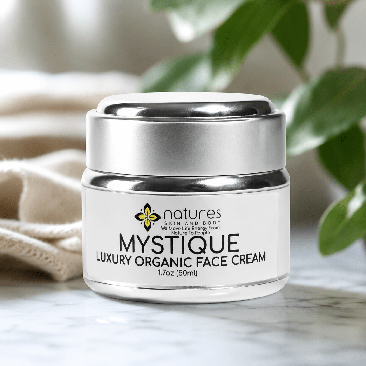 A jar of Nature's Skin and Body Mystique Luxury Organic Face Cream sits on a marble surface with a soft beige cloth and green leaves blurred in the background.